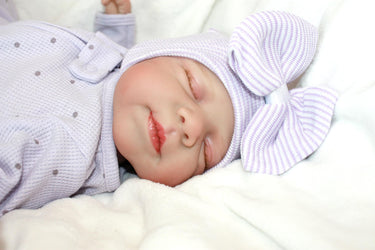 A baby lies peacefully on a soft white blanket, surrounded by a serene atmosphere.
